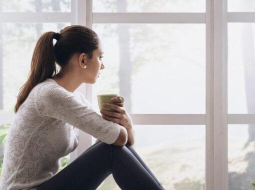 Femme assise près d'une fenêtre, buvant du café